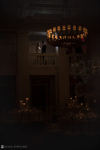 A bride and groom standing under a chandelier in the elegant Yale Club, celebrating their wedding.