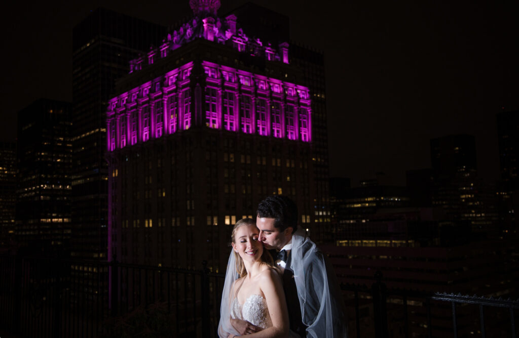 A wedding couple posing in front of the Yale Club building at night.