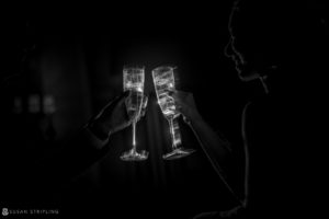 A black and white photo of a couple toasting champagne glasses at their wedding.