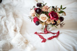 A wedding bouquet of red and burgundy flowers on a white bed at the Ritz Carlton in Philadelphia.