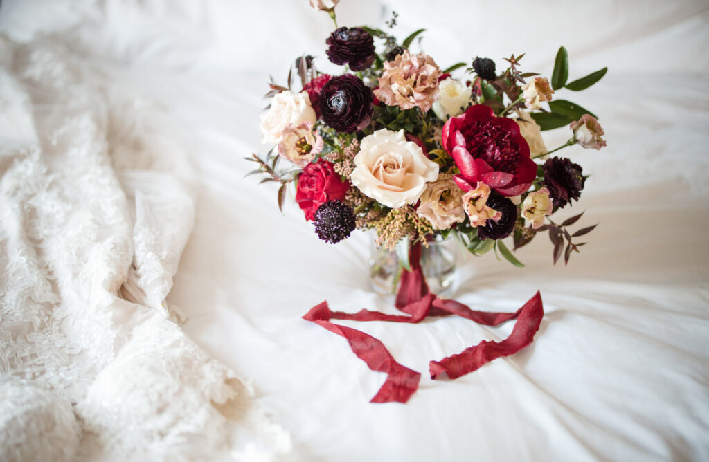 A wedding bouquet of red and burgundy flowers on a white bed at the Ritz Carlton in Philadelphia.