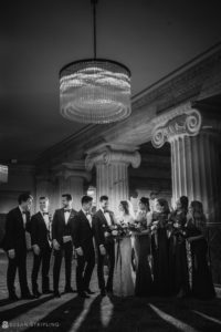 A black and white photo of a wedding party standing in front of a chandelier at the Ritz Carlton in Philadelphia.