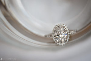 A Philadelphia diamond engagement ring sits on top of a glass.