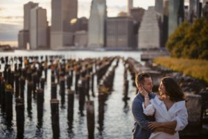 A couple embraces in front of the Manhattan skyline during their engagement session at the estate at Florentine Gardens.