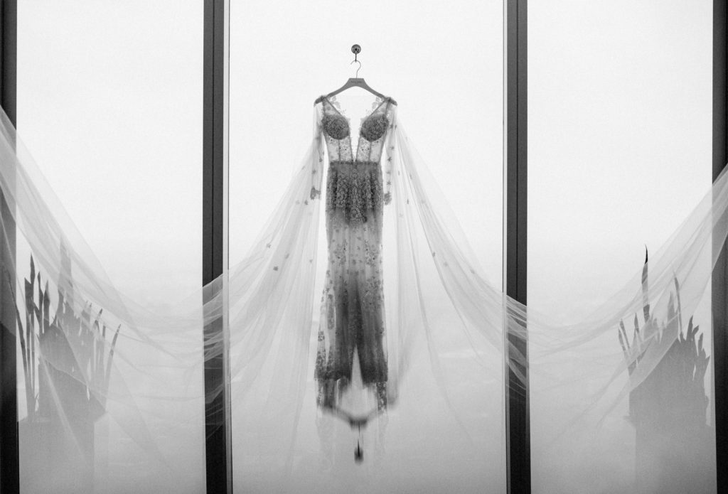 A black and white photo of a wedding dress hanging from a window at the Four Seasons Hotel Philadelphia at Comcast Center.