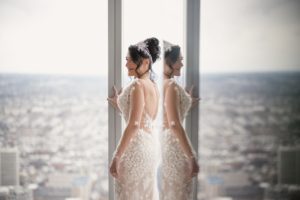 A bride in a wedding dress standing in front of a window with a view of the city at the Four Seasons Hotel Philadelphia at Comcast Center Wedding.