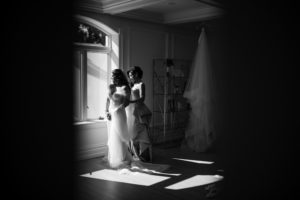 Two brides standing in front of a window at the Estate at Florentine Gardens.