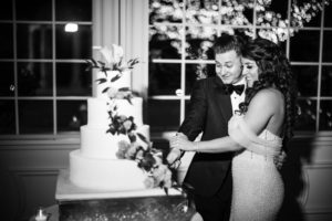 A bride and groom cutting their wedding cake at The Estate at Florentine Gardens in a black and white photo.