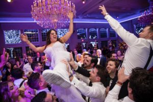 At The Estate at Florentine Gardens, a bride and groom are joyfully being thrown into the air by their excited guests during a lively wedding reception.