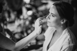A summer bride getting her makeup done in a black and white photo at the Brooklyn Botanic Garden.