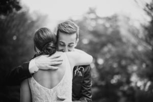 A summer bride and groom hugging in front of a tree.