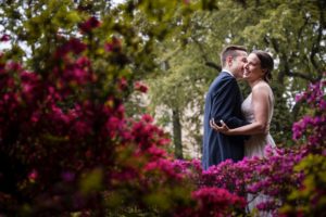 A bride and groom embrace in front of pink flowers at their summer wedding.