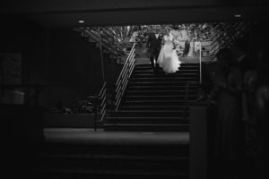 A bride and groom walking down the stairs in a dimly lit room during their summer wedding.
