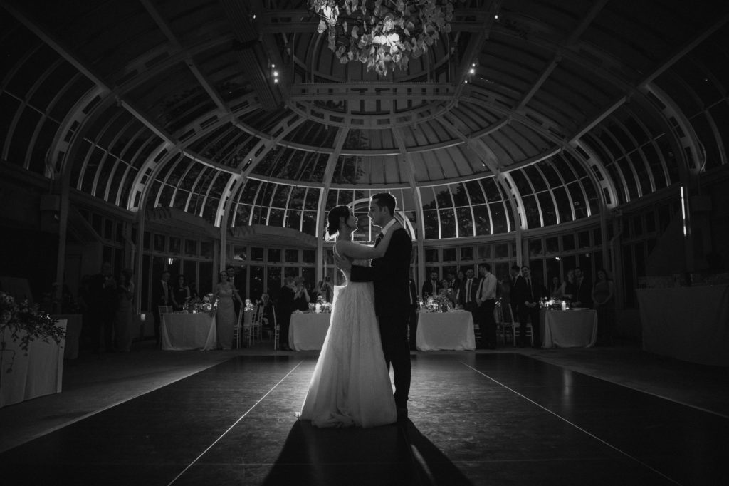 A bride and groom dance in a Brooklyn Botanic Garden conservatory at night during their wedding.
