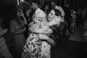 Two women joyfully hugging on the dance floor at a summer wedding.