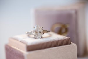 A wedding engagement ring sits on top of a box next to the Wallace and Loeb Boathouse.
