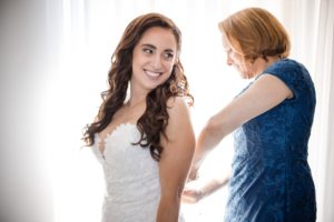 A bride is helping her mother put on her wedding dress at Wallace and the Loeb Boathouse.