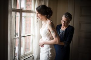 A woman is helping her daughter put on her wedding dress at Bourne Mansion during the summer.