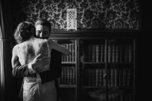 A summer wedding couple embracing in front of a bookcase at the Bourne Mansion.