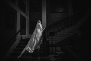 A bride is standing on a staircase in the Yale Club, a dark room beautifully lit for her wedding.
