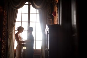 A bride and groom standing in front of a window at Bourne Mansion during their summer wedding.