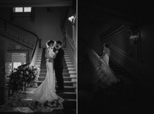 A bride and groom standing on the stairs at Bourne Mansion during a summer wedding in a dark room.