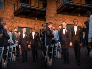 Two men in tuxedos walking down the wedding aisle at Liberty Warehouse.