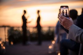 A man taking a photo of a couple at sunset during their summer wedding at Liberty Warehouse.