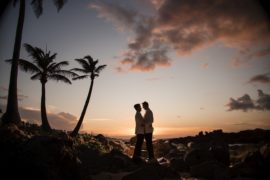 A wedding couple standing on rocks at sunset with palm trees in the background at Dorado Beach, Ritz Carlton.
