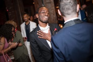 A man in a tuxedo laughing at a Liberty Warehouse party.