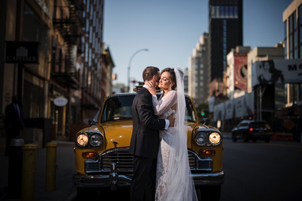 A bride and groom kiss in front of a yellow cab in NYC.