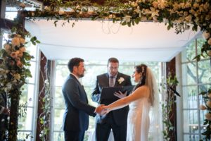 Wallace and Loeb Boathouse provides a picturesque backdrop for a memorable wedding ceremony, where the bride and groom lovingly exchange vows under an archway.