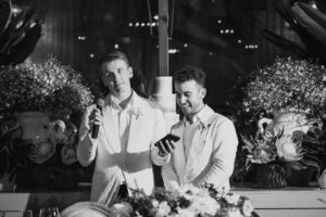 Two men in white tuxedos standing in front of a table at a Ritz Carlton wedding.