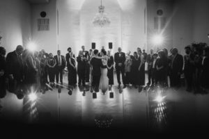 A summer wedding party stands in front of a mirror at Bourne Mansion, captured in a striking black and white photo.