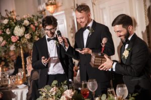 A group of men in tuxedos holding a microphone at a summer wedding reception at Bourne Mansion.