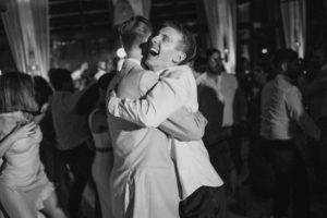 Two men embracing on the dance floor at a wedding at the Ritz Carlton.