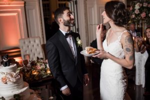 A bride and groom sharing a piece of cake at their wedding reception at Bourne Mansion during the summer.