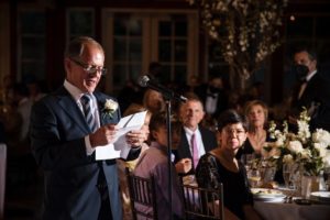 A man reading a speech at a wedding reception held at the Wallace and Loeb Boathouse.