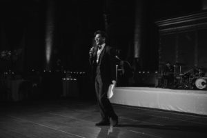 A black and white photo of a man in a suit speaking into a microphone at Capitale wedding venue in NYC.