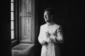 A black and white photo of a man in a white suit standing in front of a window at Gotham Hall.