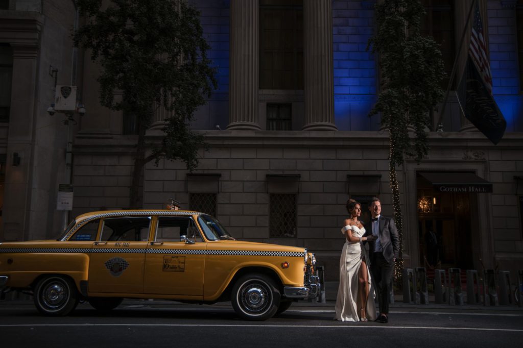 A bride and groom pose in front of a yellow cab on their wedding day at Gotham Hall.