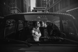 A bride and groom share a passionate kiss in the back seat of a taxi after their beautiful wedding ceremony at Gotham Hall.
