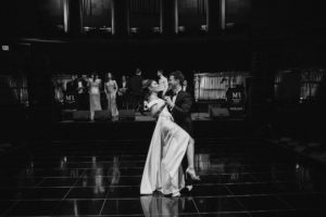 A bride and groom gracefully dancing on a stage at Gotham Hall inspires nostalgia in a captivating black and white wedding photo.