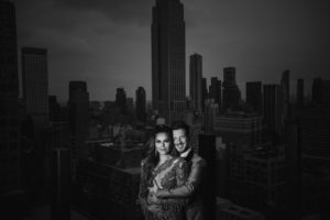 A couple posing on top of a building in New York City, capturing an enchanting moment against the backdrop of Gotham Hall.