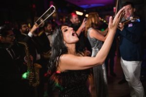 A woman is playing a trumpet at a wedding party.

or

Description: A woman is playing a trumpet at Gotham Hall party.