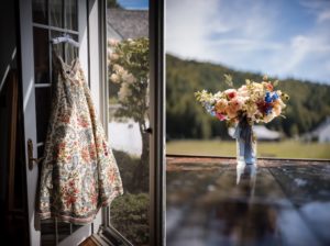 A summer wedding dress hangs on a table next to a vase of flowers at Riverside Farm.