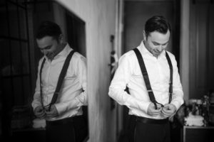 A man in Brooklyn, getting ready for a wedding by putting on suspenders in front of a mirror at 501 Union.