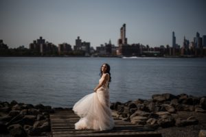 A bride standing on a dock with the city skyline in the background at 74 Wythe as part of her wedding day celebration.