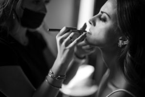 A woman is getting her makeup done for a summer wedding in a black and white photo.