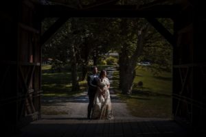 A bride and groom standing in a covered bridge at Riverside Farm during their summer wedding.